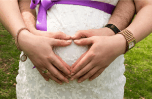 a pregnant belly, with the dads hands on the belly and the moms hands on top making the shape of a heart