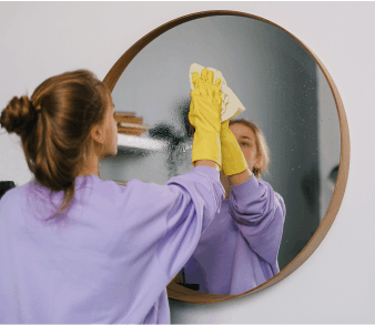 A women cleaning a wall mirror with EarthSential all purpose clove oil cleaner