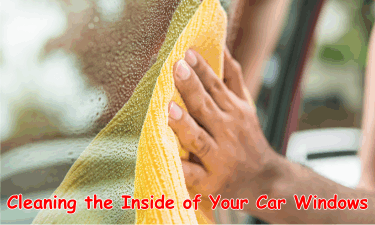 A person wiping the inside window of a car